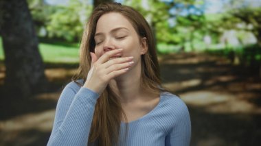 Genç beyaz kadın ormanda akıllı telefonu tutarken ağzını eliyle kapatıyor; neşeli bir eğlence..