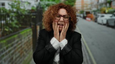 Şehirdeki İspanyol kadın, şehir ortamında, arabalarla çevrili, gözlüklü ve kıvırcık saçlı duyguları ifade eden bir iş elbisesi giymiş, hayal kırıklığı ve stres yaşıyor..