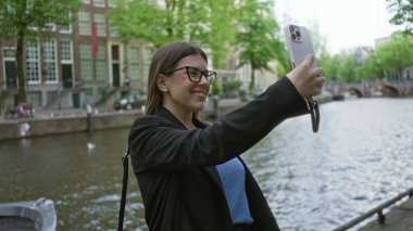 Bir kadın bahar günü Amsterdam Kanalı 'nda akıllı telefon kullanırken gülümsüyor..