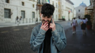 Kot ceketli, sakallı genç adam şehir sokağında telefonda konuşuyor, geçmişi bulanık..