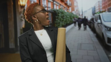 Genç Afro-Amerikalı kadın sokakta yukarı bakarken yuvarlanmış planlar üzerinde çalışıyordu..