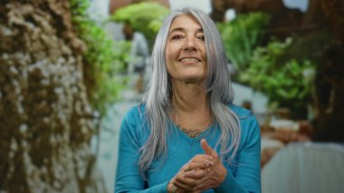 Kıdemli kadın doğal güzelliklerle çevrili yeşil bir parkta coşkulu enerjisini ve mutluluğunu sergiliyor..