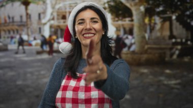 Kırmızı beyaz önlüklü ve Noel Baba şapkalı bir kadın sokakta elini uzatıyor..