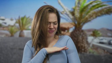 Kadın, sallanan palmiye ağaçları ve tiksintiyle dolu kıyı güneşli caddede el sallıyor..