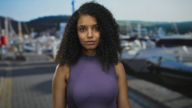 Sahil limanında, arka planda açık gökyüzünün altında kayık ve tepelerle şaşırmış bir kadın..