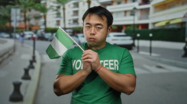 Elinde Nijerya bayrağı olan, yeşil gönüllü gömlekli arka planda bulanık şehir manzarası olan bir adam, çok kültürlü bir açık hava ortamını işaret ediyor..
