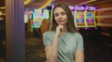 Kumarhanedeki kadın renkli kumar makinelerinin yanında otururken düşünceli bir ifadeyle ve günlük kıyafetleriyle.