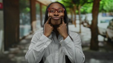 Gözlüklü bir kadın şehir caddesinde neşeli bir şekilde gülümserken yüzüne bakıp neşeli bir ifade takınıyor..