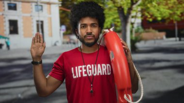 Afro saçlı bir cankurtaran elinde can simidi olan bir caddede dikiliyor ve dışarıda yemin ediyor..