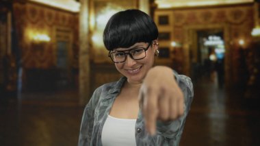 Güzel aydınlatılmış bir müzede gülümseyerek elleri ile kalp şekillendiren genç bir kadın içeride neşe ve kültürün özünü yakalıyor..