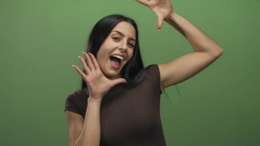 İzole edilmiş yeşil bir arka plan duvarına neşeyle gülümseyen genç bir kadın, canlı bir ortamda neşeli ifadeler sergiliyor..