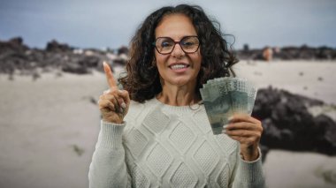 Sahilde elinde Endonezya rupiası banknotları olan bir kadın, deniz kenarındaki heyecan ve kendine güveni dile getiriyor..