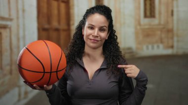 Eski bir üniversite avlusunda İspanyol bir kadın elinde basketbol topuyla kendini göstererek atletik ruhu ve akademik arkaplanı canlandırıyor..