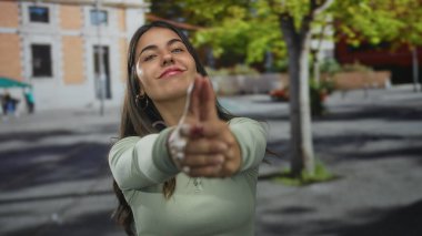 Güneşli bir günde ağaçlarla çevrili bir sokakta silah gibi neşeli bir şekilde gülümseyen bir kadın..