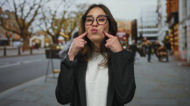 Londra 'da bir şehir caddesinde gülümseyen İspanyol kadın, gözlüklü ve beyaz gömlekli, şehir trafiği ve insanlarla çevrili..