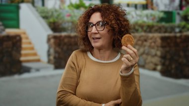 Şehir caddesinde taş duvar altyapısı olan kurabiye tutan bir kadın sıradan bir şehir ortamını işaret ediyor. İspanyol asıllı orta yaşlı bir kadın ilginç bir şekilde atıştırmanın tadını çıkarıyor..