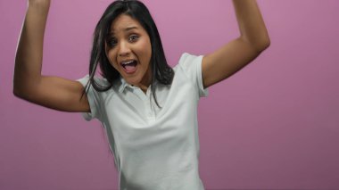 Canlı pembe bir arka plana karşı şaşırmış bir şekilde elini kaldıran bir kadın izole edilmiş bir sahnede duygu ve ifade aktarıyor..