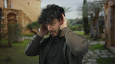 Güneşli bir günde, açık havada sakallı genç bir İspanyol kafası karışık bir ifadeyle bir jest yapıyor.