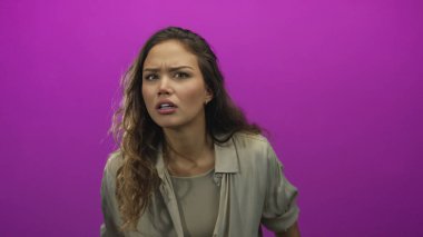 Duygularını canlı pembe arka plana karşı kaldıran kadın, tecrit ortamında sürpriz ve aciliyeti ifade eder.