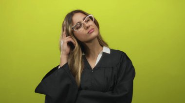 Siyah cüppeli bir kadın fotoğraf stüdyosunda gözlük takarken parmağıyla şakağına işaret ediyor..