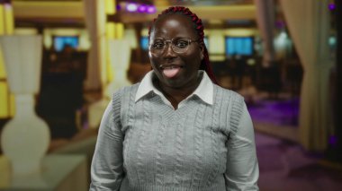 Bir otel ortamında, neşeli bir şekilde dilini dışarı çıkaran bir kadın, canlı ışıklandırma ve modern dekorla, neşeli ve esprili bir atmosfer yayıyor..