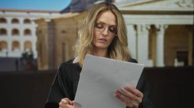 Gözlüklü genç kadın yargıç gün boyunca adliyenin önünde gazete okuyor..