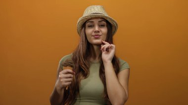 Şapka takan genç bir kadın turuncu arka planda dondurma tutuyor. Kendine güvenen bir ifadeyle yaz ve tatil havası veriyor..