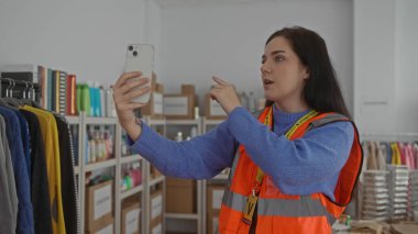 Gönüllü odasında turuncu yelek giyen ve iç mekanda bağış ortamını geliştiren kıyafetler ve kutularla dolu bir kadın aranıyor.