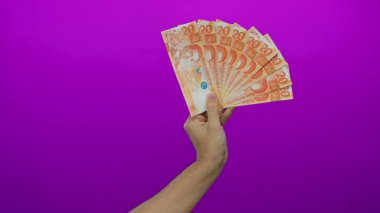 Beyaz adamın elinde Filipinli peso banknotları, parlak mor bir arka plan, sergilenen finansal kavramlar ve para birimi odaklı.