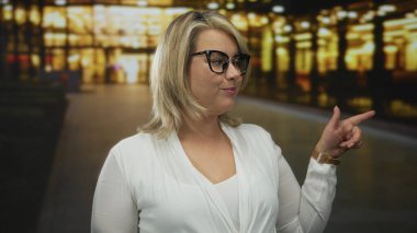 Kadın telefon şeklindeki elini kulağına doğru tutuyor ve bulanık şehir ışıklarıyla dolu yoğun bir caddede parmaklarını işaret ediyor; iletişim bağlantıları neşeli.