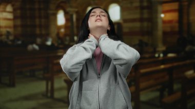 Boyun ağrısı çeken bir kadın loş bir Katolik kilisesinde, ahşap banklarla dikilirken..