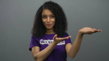 Stüdyoda gri duvara karşı gönüllü tişört giyen genç bir kadın..