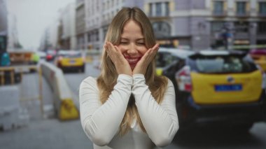 Sarışın ve ağzı açık genç bir kadın, şehir inşaatında el ele tutuşarak, şaşkınlık verici bir şaşkınlık yaşıyor..