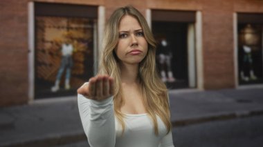 Uzun düz sarı saçlı, beyaz bluzlu, caddede parmakla gösteren bir kadın. Hayal kırıklığı uyarısı..