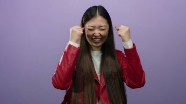 Kırmızı ceketli bir kadın, izole edilmiş mor arka planda kutlama yapıyor. Stüdyo ortamında sevinç ve heyecan ifade ediyor..