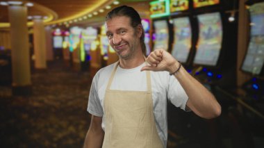 Önlüklü, uzun sarı saçlı bir adam binadaki kumar makinelerinin yanında baş parmak hareketi yapıyor. Onaylamıyor..