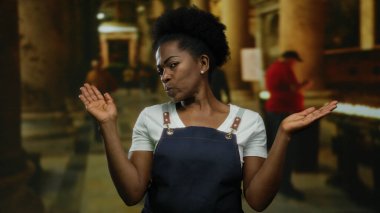 Önlük giymiş bir kadın kilisede yetişmiş, kapalı bir dini ortamda, bulanık figürler ve mumlarla çevrili bir şekilde tefekküre dalmış..