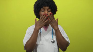 Beyaz önlüklü ve steteskop kullanan kadın doktor yeşil stüdyoda elleriyle öpücük hareketi yapıyor..