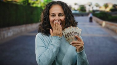 Orta yaşlı bir kadın elinde Meksika pezosu ile şehir caddesinde sürpriz bir ifadeyle geziyor..