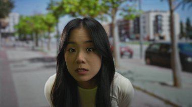 Şehir dışındaki uzun saçlı, güneşli bir günde arka planda bulanık ağaçlar ve binalarla eğlenen bir kadın.