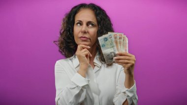 Soyutlanmış mor bir geçmişe karşı elinde İngiliz sterlinli banknotlar tutan orta yaşlı bir kadın, finansal değerlendirmeyi öneriyor..