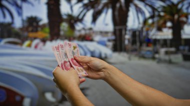 Park halindeki arabalarla Meksika pesolarını elinde tutan adam para değişimi, iş ve yatırım fırsatlarını temsil ediyor..