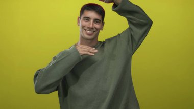 İspanyol adam gülümseyen pozlar verirken elleri sıradan, canlı, sarı bir stüdyo ortamında; neşe.