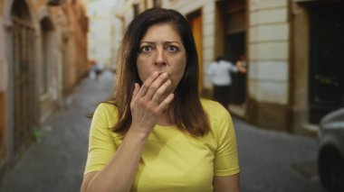 Orta yaşlı, kaygılı bir ifadeyle İspanyol kadın güneş ışığıyla aydınlanan kaldırım taşı caddesinde ağzını kapatıyor. Sürpriz..