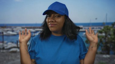 Mavi şapkalı ve gömlekli kurye kadın liman teknelerinin yanındaki bir sokakta iki elini kaldırdı..