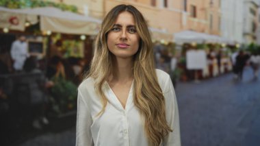 Genç sarışın kadın, dışarıdaki kafede iki elini de kameraya doğru sallıyor. Dikkat dostluğu bağlantısını selamlıyor..