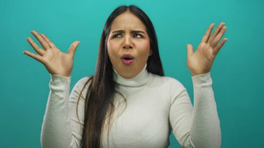 İzole edilmiş yeşil arka planda anlamlı jestleri olan beyaz bir kazak giyen, elleri ve yüz ifadeleriyle şaşkınlık ve şaşkınlık duyguları gösteren bir kadın..