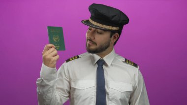 Genç İspanyol pilot yeşil bir pasaport tutuyor canlı pembe bir arka plana karşı, kendine güvenen bir ifadeyle üniforma giymiş..