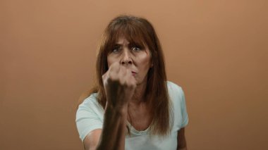 Beyaz gömlekli yaşlı bir İspanyol kadın, kızgın bir şekilde yumruğunu sıkı bir kahverengi duvara dayamış, kapalı bir ortamda duygularını ve gücünü aktarıyor..