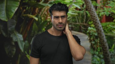 Genç Hispanik adam orman yolunda boyun ağrısı içinde, servikal bölgesini gergin bir duruşta tutuyor;.